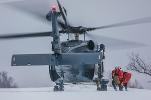Dwaj mężczyźni biegną w kierunku policyjnego śmigłowca stojącego na zaśnieżonym lądowisku.
