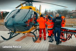 Medycy i policjant transportują poszkodowanego do śmigłowca