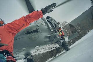 Goprowiec z poprzedniego zdjęcia rozkłada ręce na boki sygnalizując pilotowi Black Hawka zakończenie procedury lądowania, z otwartych drzwi maszyny wychyla się instruktor GOPR-u.