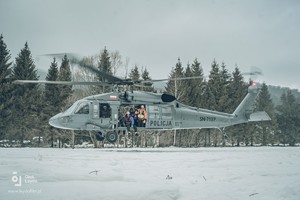 Pokryta śniegiem połonina. Policyjny Black Hawk staruje, w otwartych drzwiach maszyny ratownicy górscy.