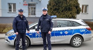 dwóch umundurowanych policjantów stoją przy radiowozie