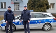dwóch umundurowanych policjantów stoją przy radiowozie