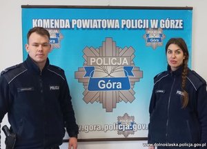 W pomieszczeniu policjanci w mundurach przy plakacie Komendy Powiatowej Policji w Górze
