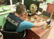 policjant siedzi przy stole na którym stoją odzyskane naczynia liturgiczne