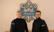 Dwóch policjantów w mundurach stojących przed gwiazdą policyjną z napisem Żmigród