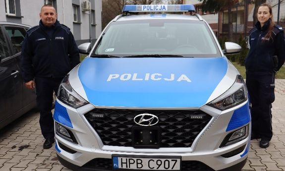 Na zdjęciu dwaj policjanci stojący koło radiowozu