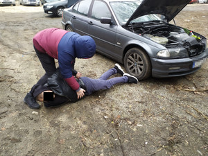 Zatrzymana osoba podejrzana o kradzież samochodu leży na ziemi a nad nią stoi nieumundurowany policjant