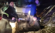 zatrzymany mężczyzna w kajdankach siedzi na ziemi, obok niego stoją funkcjonariusze, w tle skradziony pojazd