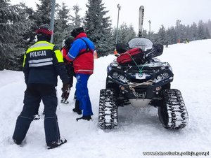 policyjny patrol narciarski pomaga poszkodowanej kobiecie na stoku