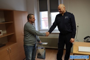 I Zastępca Komendanta Powiatowego Policji w Lubinie p.o. podinsp. Marek Szczepański gratuluje mężczyźnie bohaterskiej postawy, mężczyzna trzyma w ręku list gratulacyjny i upominek
