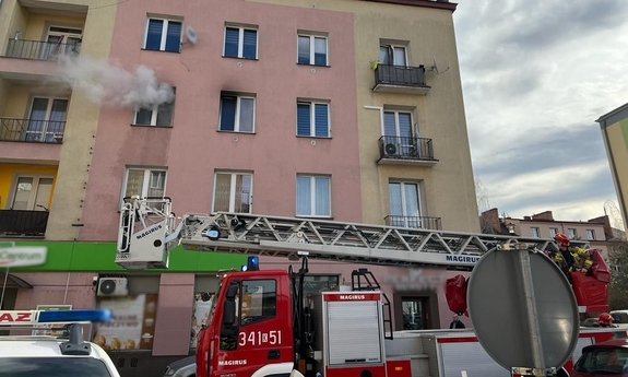 wóz straży pożarnej przed budynkiem, z okna na drugim piętrze wydobywa się dym