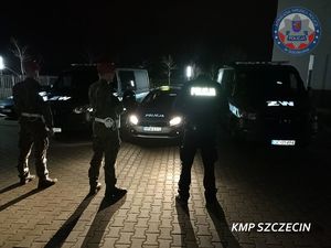 pora nocna policjant i dwaj funkcjonariusze Żandarmerii Wojskowej stoją na przeciwko zaparkowanych przed nimi radiowozu policji i dwóch samochodów żandarmerii