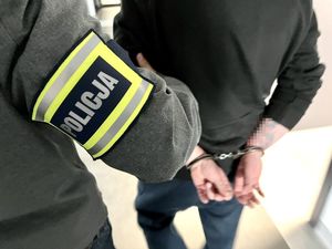 policjant prowadzi zatrzymanego, który ma ręce skute z tyłu kajdankami