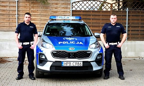 umundurowani policjanci stoją przy policyjnym radiowozie