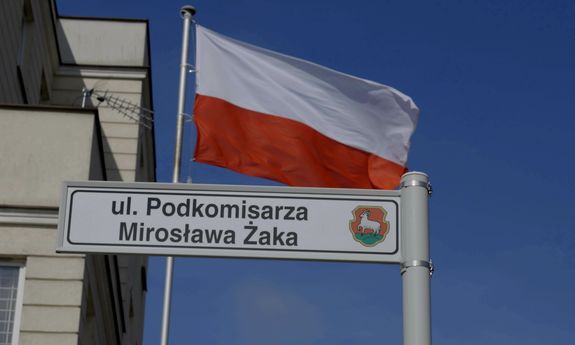 powiewająca flaga Polski oraz tabliczka z nadaną nazwą ulicy &quot;podkomisarza Mirosława Żaka&quot;