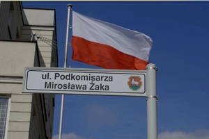 powiewająca flaga Polski oraz tabliczka z nazwą ulicy &quot;podkomisarza Mirosława Żaka&quot;