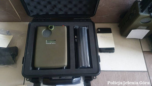 Zdjęcie przedstawia sprzęt zabezpieczony w trakcie prowadzonych działań w postaci czarnej walizki, w której znajdują się inne przedmioty o różnych wielkościach.