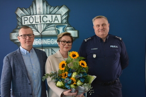 dwaj mężczyźni w tym jeden policjant stoją razem z kobietą, która trzyma kwiaty