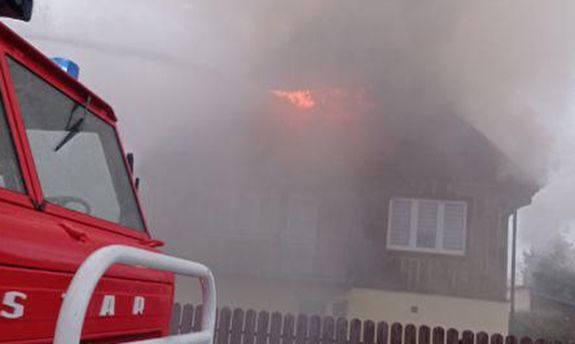 wóz strażacki, w tle płonący budynek mieszkalny