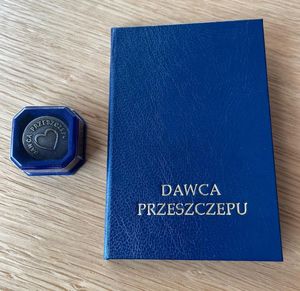 Zdjęcie przedstawia niebieską książeczkę z napisem na okładce DAWCA PRZESZCZEPU, obok niej widać małe opakowanie.