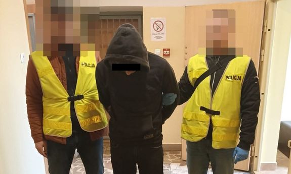 Zdjęcie przedstawia dwie osoby ubrane w odblaskowe kamizelki. Pomiędzy nimi stoi osoba ubrana na ciemno, której część twarzy zasłania czarny prostokąt.
