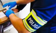 ręka policjanta z opaską odblaskową z napisem POLICJA oraz ręka zatrzymanego w trakcie wykonywania odcisków linii papilarnych