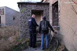 Policjant i mężczyzna z rowerem obok opuszczonego budynku