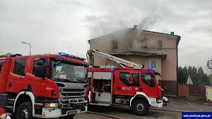 Pożar domu wielorodzinnego , przed budynkiem stoją dwa wozy strażackie