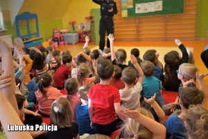 dzieci siedzące na podłodze, przed nimi stoi policjantka