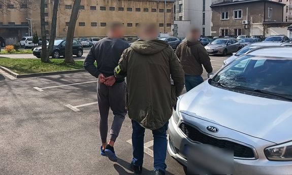 dwaj policjanci prowadzą zatrzymanego do samochodu