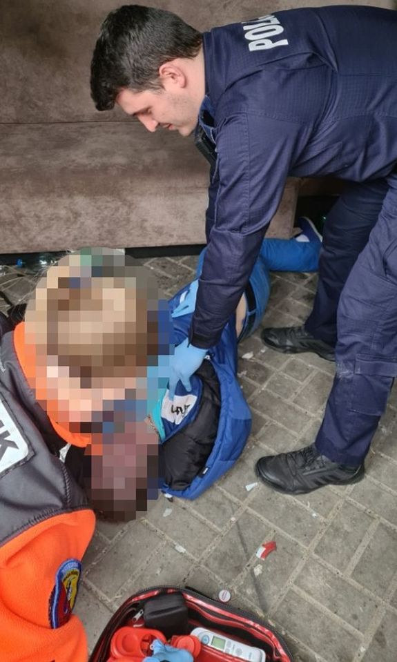 Zdjęcie przedstawia umundurowanego policjant, który pochyla się nad mężczyzną leżącym na ziemi.