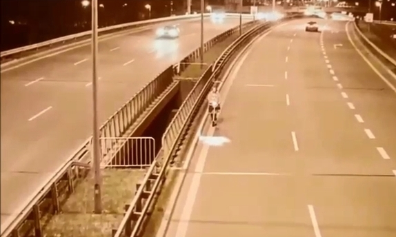 dwie trójpasmowe jezdnie drogowej trasy średnicowej. Pasem po prawej jedzie osoba na hulajnodze