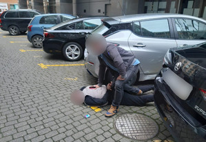 zatrzymany mężczyzna w asyście nieumundurowanego policjanta obok samochodu