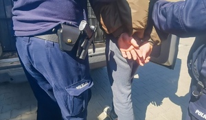 policjanci prowadzą zatrzymaną osobę, która ma na rękach kajdanki