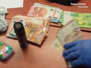 policjant liczy zabezpieczone banknoty, na stole leżą pliki z banknotami euro