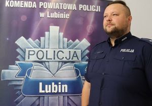 umundurowany policjant stoi na tle ścianki z napisem Komenda Powiatowa Policji w Lubinie