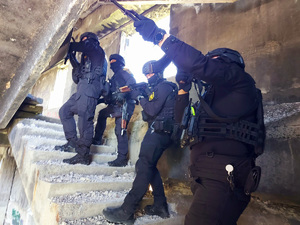 Antyterroryści na schodach w opuszczonym budynku z bronią gotową do strzału.