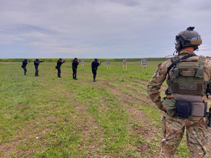 Policyjny kontrterrorysta obserwuje grupę ćwiczącą strzelanie do tarczy.