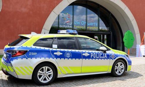 Radiowóz policyjny w tle widać budynek i napis na szklanych drzwiach: 10 lat Dni Otwartych.eu i Dni Otwarte Funduszy Europejskich