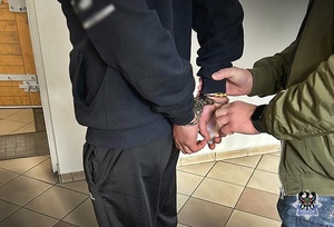 policjant zakłada kajdanki na ręce zatrzymanego