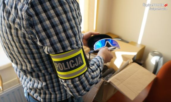 nieumundurowany policjant z opaską policja na ramieniu trzyma w ręku podrobione okulary jednej ze znanych firm sportowych