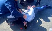 policjanci kucają nad zatrzymanym mężczyzną leżącym na ziemi i zakładają mu kajdanki na ręce