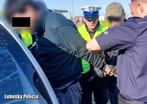 Zatrzymany mężczyzna ma zapinane kajdanki na ręce przez policjantów