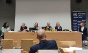 prelegenci Ogólnopolskiej Konferencji Światowej Organizacji Zdrowia siedzą za stołem prezydialnym. Jedna z nich przemawia do zebranych na sali