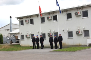 sześciu policjantów stoi przy dwóch masztach z flagami Polski i NATO