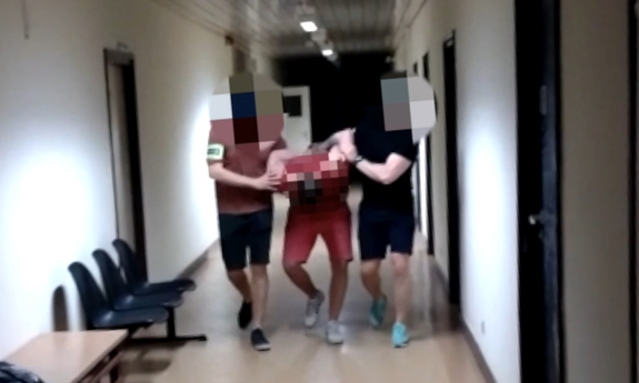 dwaj nieumundurowani policjanci prowadza zatrzymanego mężczyznę zakutego w kajdanki