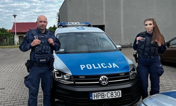 Policjanci w mundurach stojący na te radiowozu
