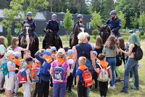 Policjanci na koniach służbowych przed nimi grupa dzieci.