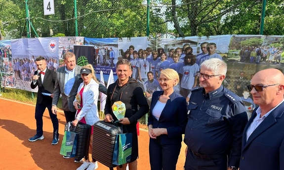 organizatorzy turnieju oraz uczestnicy z nagrodami stoją w szeregu na skraju kortu tenisowego