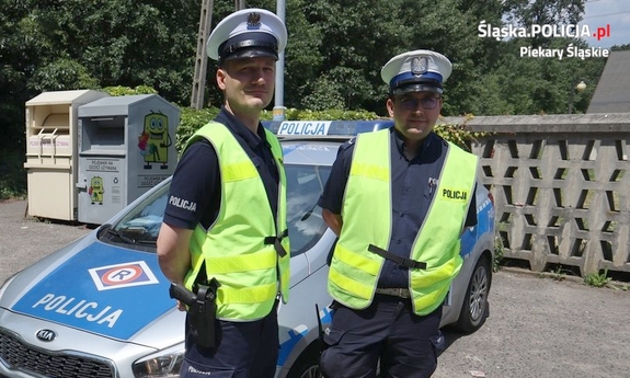 policjanci stojący obok oznakowanego radiowozu